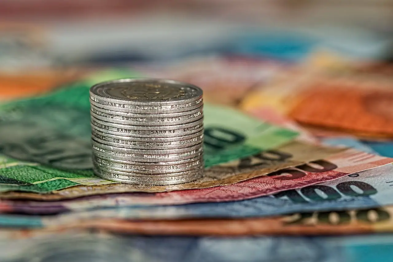 pexels-photo-210574-1 A stack of coins on top of various colored banknotes, symbolizing finance and currency.